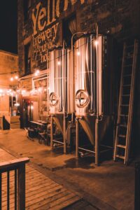 Industrial brewery exterior at night with conical fermenters and string lights