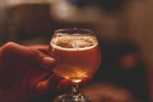 Vibrant close-up of a hand holding a foamy glass of ale indoors, perfect for celebration themes.